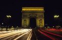 Night view of the Arc de triomphe in Paris, France with streaked lights from passing automobiles.