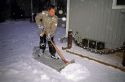 Young boy wearing winter coat shovels snow from the sidewalk.