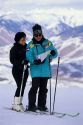 A couple snow skiing with sun glasses and nylon waterproof clothing.