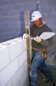 A mason uses a mason line and level to line up course with cinder block wall.