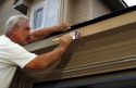 A painter applies paint to the the outside trim of a new home using a paint brush.