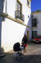 A woman pushing a baby buggy along a narrow residential street in Ronda, Spain.