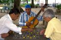 Man playing a guitar watches a checker game at a park in Rio de Janeiro, Brazil.