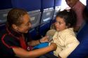 Flight attendant helping a child buckle her seatbelt on an airplane in Argentina.