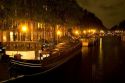 Boats docked at night along a canal near the Amstel River in Amsterdam, Netherlands.