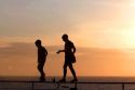 Silhouette of children walking on a railing at sunset by the sea.