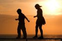 Silhouette of children walking on a railing at sunset by the sea.