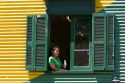 Woman looking out the window of a colorful building in the La Boca barrio of Buenos Aires, Argentina.