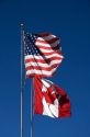 The Flag of the United States of America and the National Flag of Canada stand together on the international border at Port Huron, Michigan and Point Edward, Ontario.