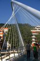 People walk across the Zubizuri Footbridge spanning the Nervion River in Bilbao, Biscay, Basque Country, northern Spain.
