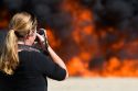 Female photographer taking digital photos of a jet fuel fire at a firefighter airport training facility in Boise, Idaho, USA. MR