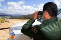United States Border Patrol agent using binoculars to survey the new border fence that prevents illegal immagrant crossings at the U.S./Mexico border near San Diego, California