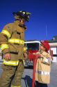 7 year old boy looks up to a firefighter while dressed in his home made Halloween costume as a firefighter in Boise, Idaho, USA.