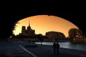 View of the Notre Dame cathedral at sunset through the arch of the Tournelle Bridge on the River Seine in Paris, France.