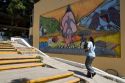 Mexican college student walking in front of a mural on the campus of Universidad Autonoma de Guerro located in Acapulco, Guerrero, Mexico.
