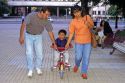 Parents helping child ride a tricycle in Santiago, Chile.
