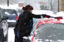 Woman brushing snow off of a car in Boise, Idaho, USA.